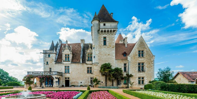 Aussenansicht des Schosses "Chateau des Milandes" vor dem Schloss wachsen bunte Blumen und der Himmel ist blau