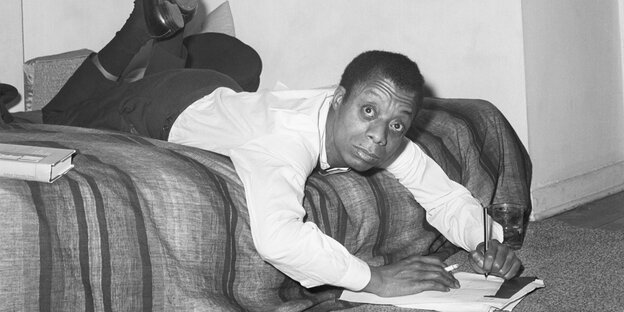 In einer scheinbar unbequemen, aber tatsächlich bequemen Schreibposition breitet sich der Schriftsteller James Baldwin in seiner New Yorker Wohnung auf dem Bett aus, um einige Notizen zu machen.