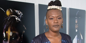 Eine Schwarze Frau mit hochgesteckten Haaren vor Fotografien Schwarzer Frauen
