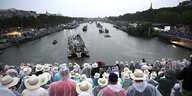 Blick von einer Brücke mit vielen Zuschauern mit Kopfbedeckung auf die Seine, auf der Schiffe fahren
