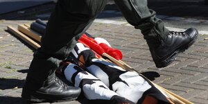 Zu sehen sind Beine von einem Polizisten, der über zusammengerollte Fahnen geht