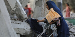Eine Frau sammelt Klamotten aus den Trümmern eines Hauses