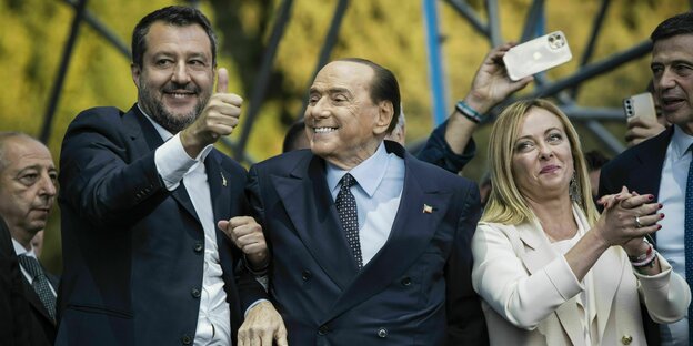 Matteo Salvini, Silvio Berlusconi und Girogia Meloni stehen auf einer Bühne. Salvini stützt dabei den rechten Arm von Berlusconi und reckt den Daumen in Richtung Kameras