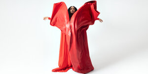 Die Soulsängerin Y'akoto posiert in einem voluminösen roten Outfit und ausgebreiteten Armen