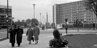 Das Schwarzweißfoto zeigt vier Spaziergänger*innen, im Hintergrund sieht man ein modernes Wohnhochhaus mit Balkonen