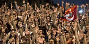 Viele Menschen recken ihre Hände in die Luft, einer schwenkt eine Türkei-Fahne