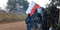 Bewaffnete vermummte Polizisten an einem Grenzzaun mit polnischer Flagge