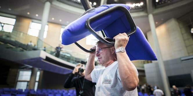 Ein Mann trägt einen Stuhl im Bundestag