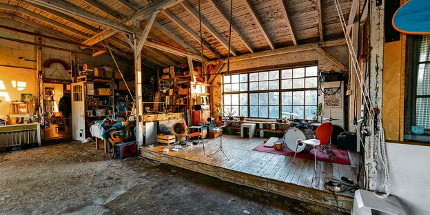 Ein Raum mit einer Bühne aus Holz vor einem alten Fabrikfenster. Auf der Bühne steht unter anderem ein Schlagzeug.