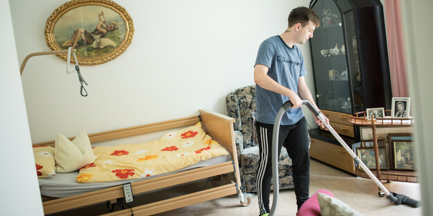 Ein junger Mann hantiert mit dem Staubsauger in dem Zimmer einer alten Person