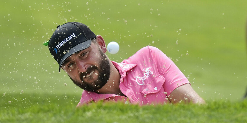 Aufgrund der hohen Grasnarbe sieht man nur den Kopf von Stephan Jäger, einen Golfball und auffliegenden Sand