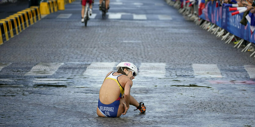 Triathletin sitzt nach einem Sturz vom Rad auf der nassen Straße