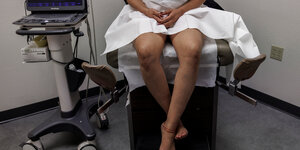 Eine Frau sitzt auf einem gynäkologischen Stuhl, ihr Unterleib ist abgedeckt