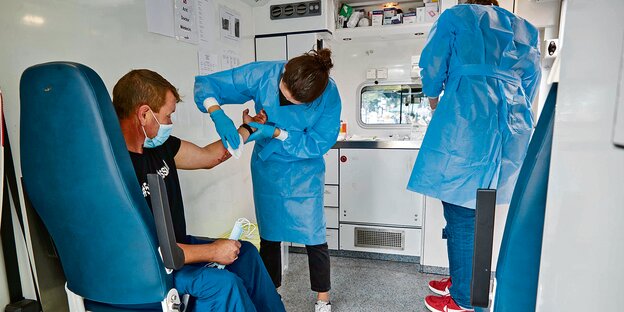 Ein Patient wird von zwei Personen in blauen Kitteln versorgt.