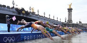 Schwimmerinnen springen in die Seine, dahinter eine Brücke
