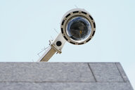 Eine runde Videoüberwachungskamera - von unten fotografiert - ragt über einen Vorsprung.