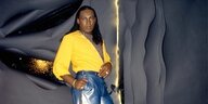 Sylvester James lehnt in gelbem Hemd an eine Wand