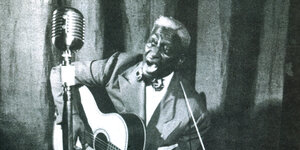 Der Sänger Lead Belly sitzt mit einer Gitarre vor einem Mikrofon.