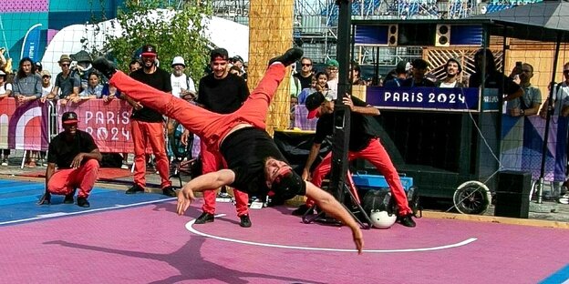 Breakdancer in Paris auf einem öffentlichen Platz.Die Männer tragen rote Hosen und schwarze Shirts und tanzen athletisch