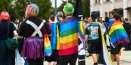 Junge Menschen stehen auf einem Platz, manche haben sich Regenbogenflaggen um die Schultern gelegt, eine Person trägt eine Weste mit der aufschrift: Protect Trans Kids