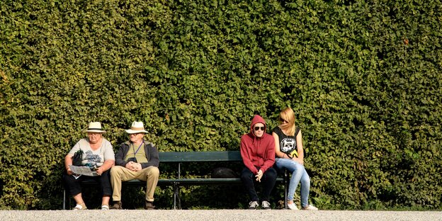 Eine Bank mit vier Menschen vor einer hohen grünen Hecke