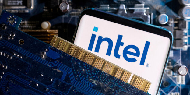 Leuchtender Smartphone Bildschirm mit blauem Intel-Logo auf weißem Hintergrund. Das smartphone liegt auf einem Haufen Chips und Prozessorenteile des Chipherstellers.