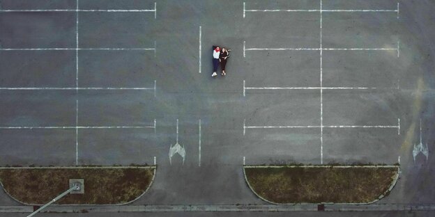 Drohnenaufnahme: Ein Paar liegt auf dem Asphalt eines Parkplatzes