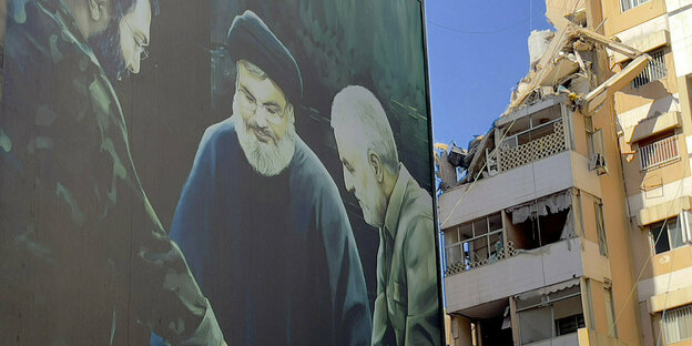 Ein Plakat mit dem verstorbenen Hisbollah-Militärkommandeur Imad Mughnijeh (l-r), Hisbollah-Führer Sajjid Hassan Nasrallah und dem verstorbenen General der Revolutionsgarden Kassem Soleimani ist in der Nähe eines beschädigten Gebäudes zu sehen, das bei einem israelischen Luftangriff in Beirut getroffen wurde.