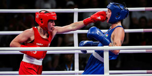 Eine rot bekleidete Boxerin boxt einer blau bekleideten Boxerin ins Gesicht