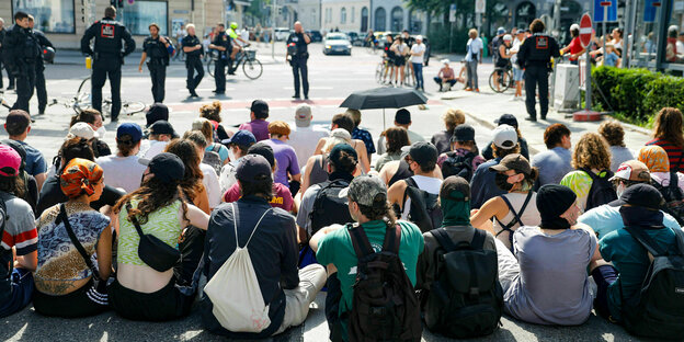 AktivistInnen sitzen auf einer Strasse, sie sind von hinten zu sehen