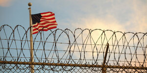 Stacheldraht auf einem Zaun, dahinter weht eine US-Flagge
