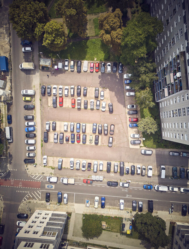 Ein Parkplatz aus der Vogelperspektive mit vielen Autos und dem mobilen Nachbarschaftstreff Kleiner Frieder am Rand bei den Kastanien