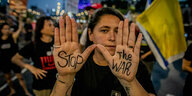 Eine junge Frau zeigt während einer Kundgebung die Innenflächen ihre Hände, auf denen "Stop the War" geschrieben steht.
