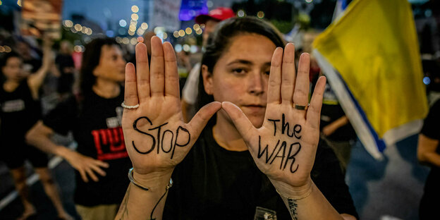 Eine junge Frau zeigt während einer Kundgebung die Innenflächen ihre Hände, auf denen "Stop the War" geschrieben steht.