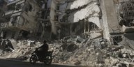 Ein Motorrad fährt an den zerstörten Gebäuden Aleppos vorbei.