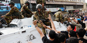 Soldaten reichen Demonstranten die Hände von einem Panzer aus