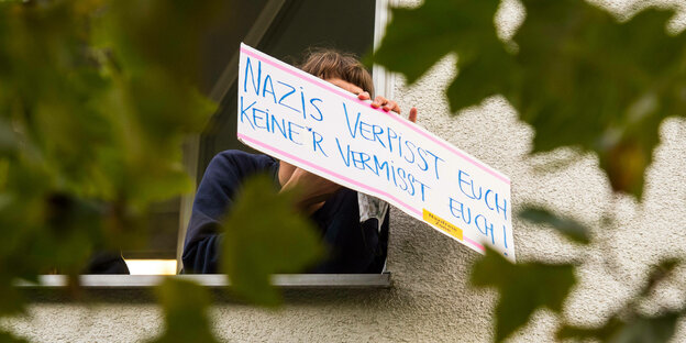 Aus dem Fenster einer Wohnung hält eine Person ein Schild mit der Aufschrift 