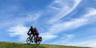 Zwei Personen fahren auf einem Tandem vor einem blauen Himmer