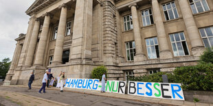 Unterstützer der Volksinitiative "Hamburg soll Grundeinkommen testen!" bauen vor dem Hanseatischen Oberlandesgericht ein Banner mit der Aufschrift "Hamburg nur besser" auf.