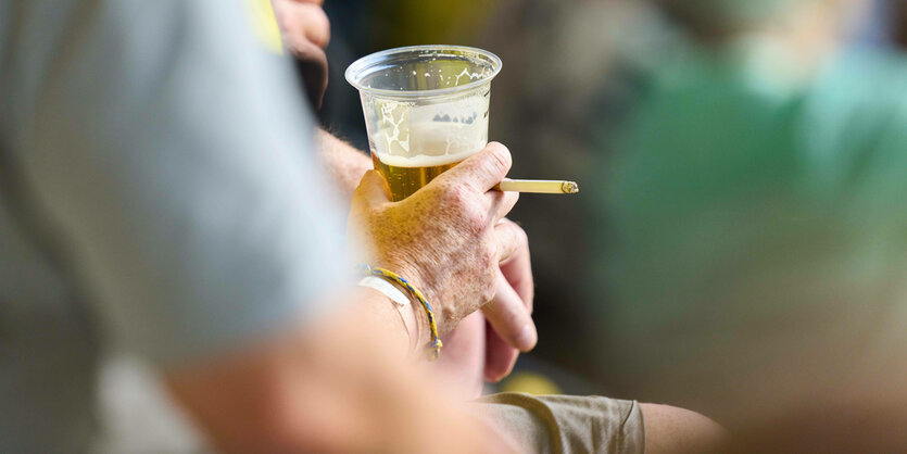 Eine Person hält ein Bier und eine Zigarette in der Hand.