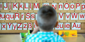 Ein Kind sitzt vor einer Tafel mit Buchstaben.