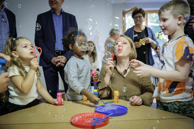 Familienministerin Lisa Paus pustet mit Kindern in einer Kita Seifenblasen in die Luft.