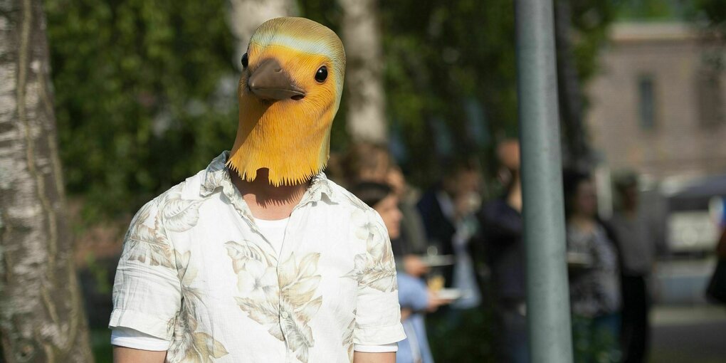 Ein Mann steht mit einer gelben Vogelmaske auf dem Kopf zwischen Bäumen