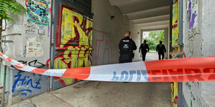 In einem mit Flatterband abgesperrten Hauseingang stehen drei Polizisten