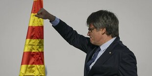 Puigdemont reckt die Faust nach oben, im Hintergrund die gelb-rote Fahne.