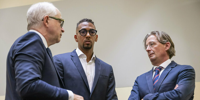 Drei Männer in Anzügen, in der Mitte steht Jérôme Boateng und blickt in die Kamera.