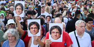 Menschen halten sich Bilder von Puigdemont vor ihre Gesicht