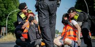 Polizisten entfernen zwei Demonstranten, die sich auf der Straße festgeklebt haben