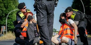 Polizisten entfernen zwei Demonstranten, die sich auf der Straße festgeklebt haben