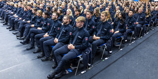 Absolventen der Polizeiakademie in Uniform sitzen bei ihrer Abschlussfeier in einer großen Halle